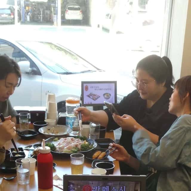 식당 테이블에서 휴대폰 화면을 함께 보며 디지털 홍보를 안내하는 장면