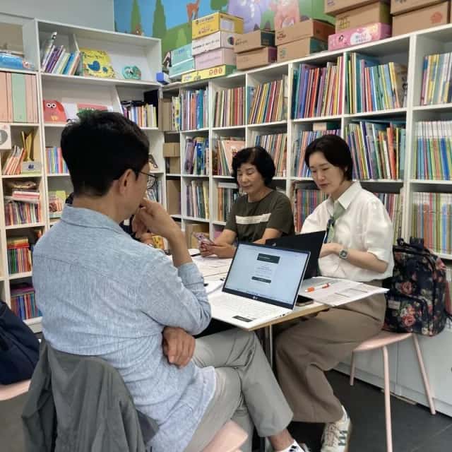 어린이 도서관에서 노트북을 펴고 담당자와 AI 활용 방안을 상담하는 컨설턴트